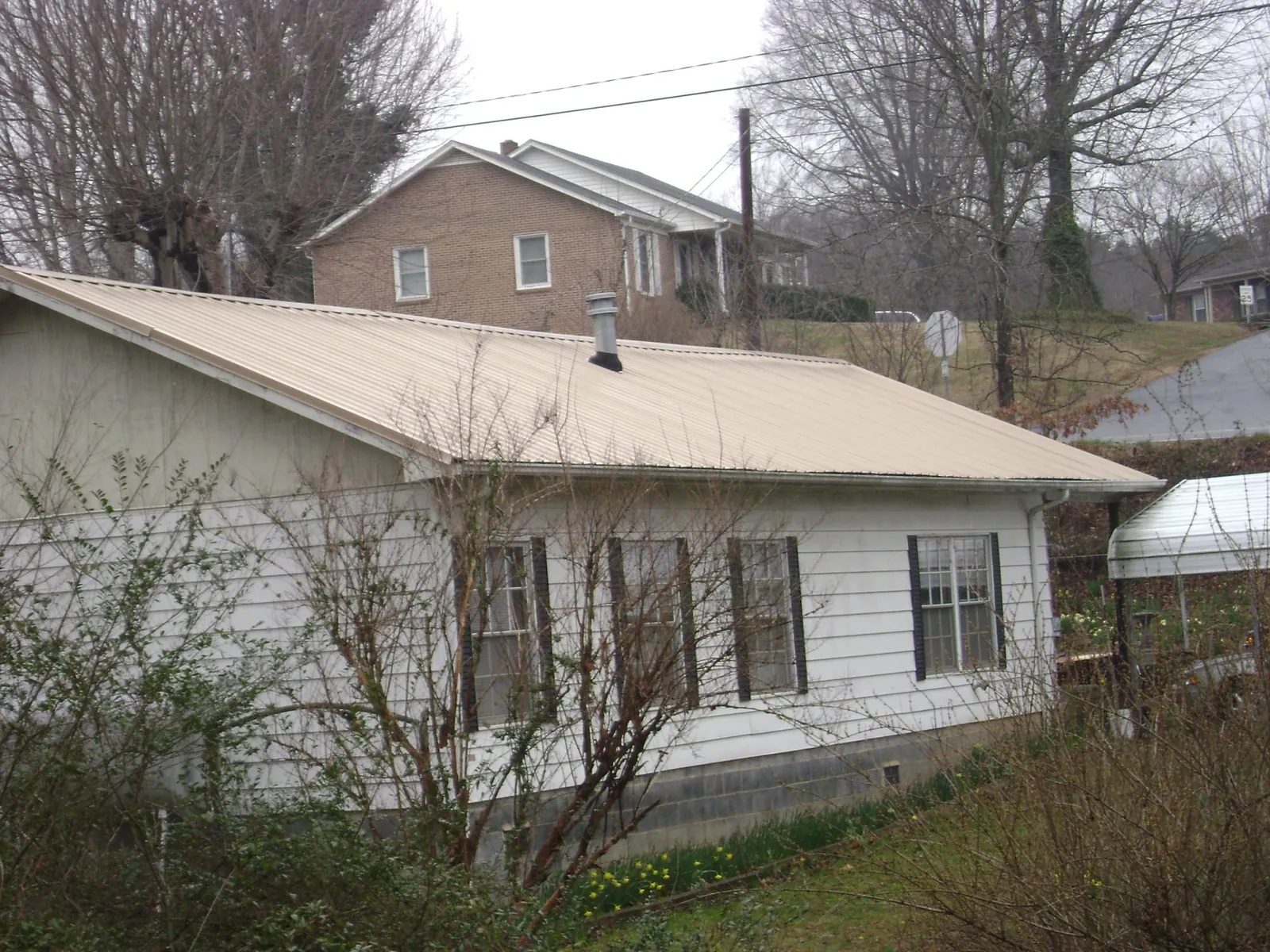 Tan metal roof on a white sided house set into a hillside — Commercial Roofing by Roofing Brothers in Paris